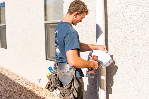 Radon mitigation fan being installed on the side of an arizona home by a professional.